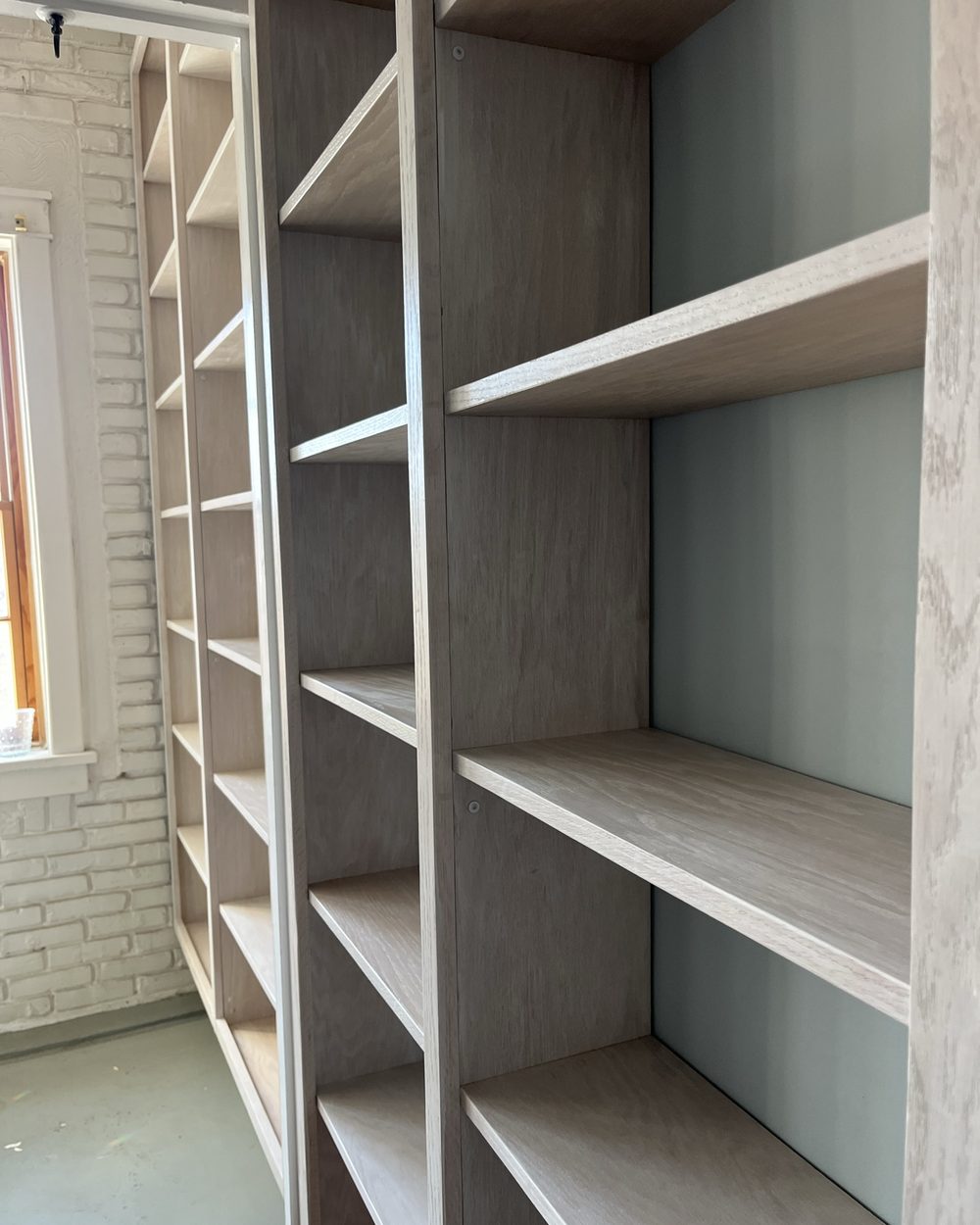 White floor to ceiling built-in shelving beside a painted brick wall