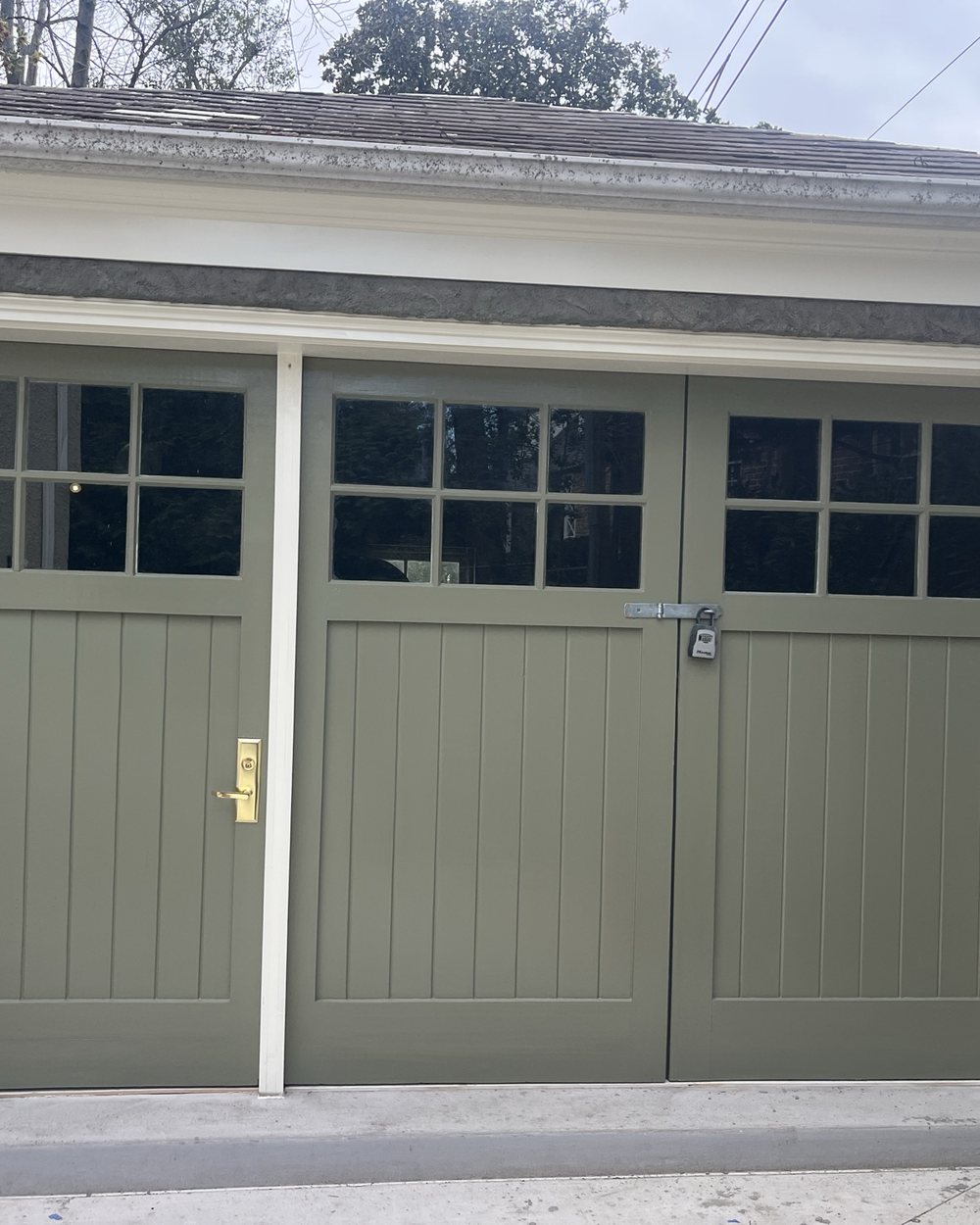 Sage green custom carriage-style garage doors with divided-light windows and brass hardware