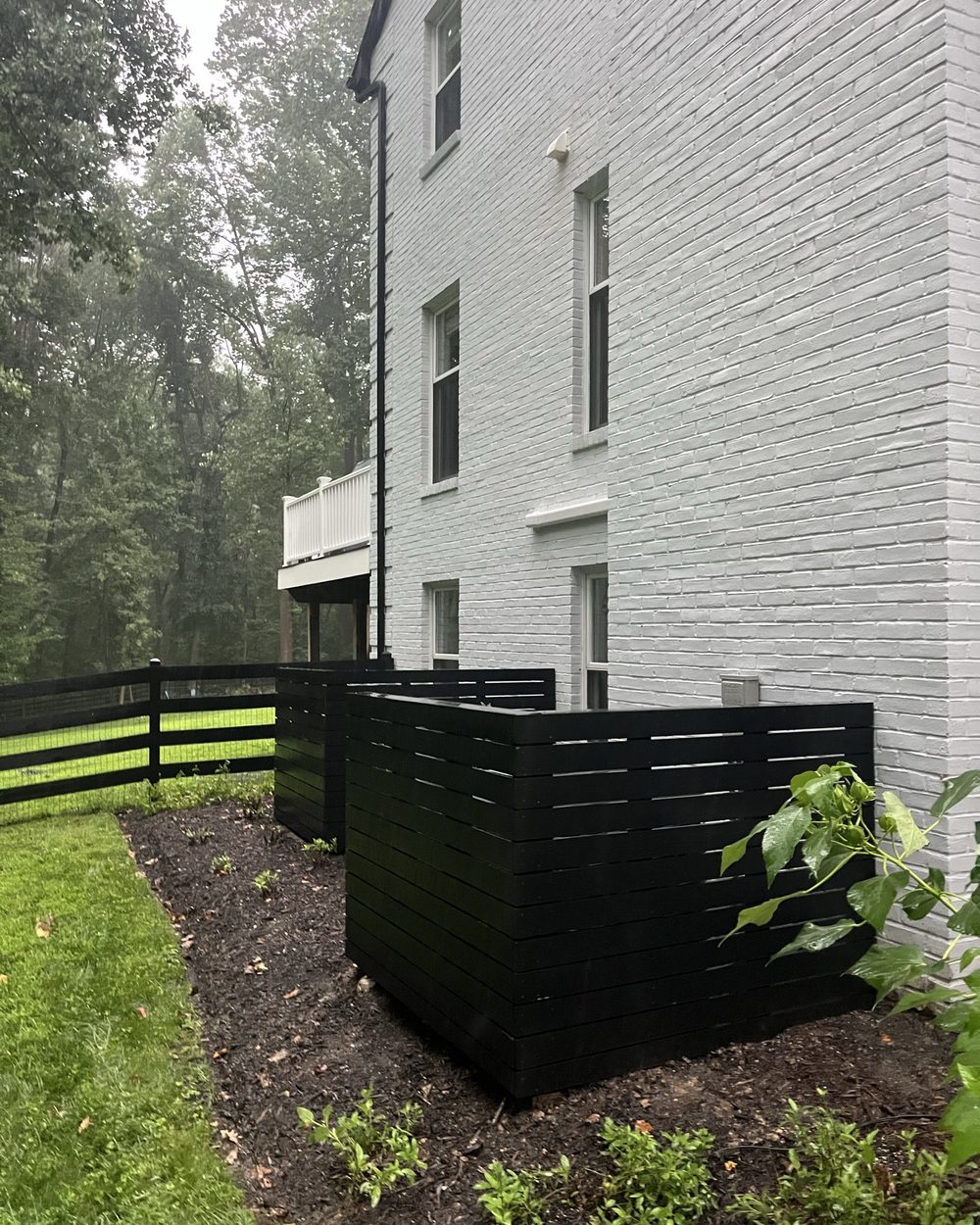 Black slat enclosure installed beside a white brick house
