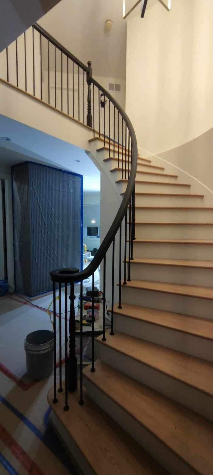 Curved staircase with restored wood treads and black metal railing during a full interior renovation